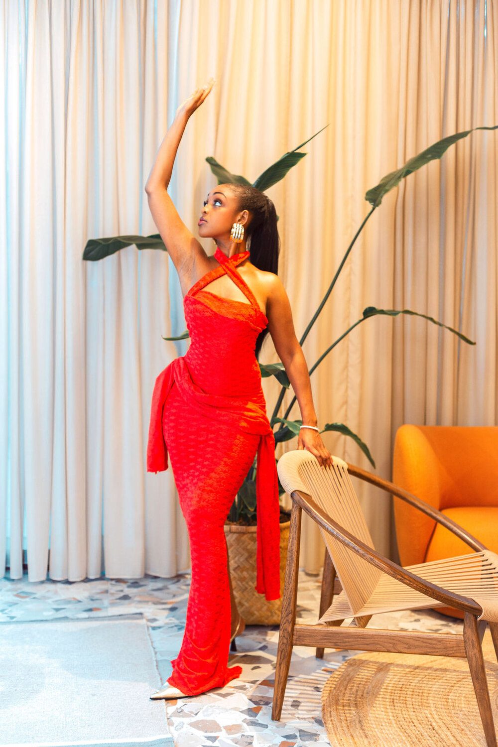 The Esther Royale Gown in red &mdash; arm raised, sash held
